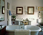Freistehende Badewanne in weißem Landhaus-Badezimmer mit antiken Möbeln und halbhoher Wandverkleidung