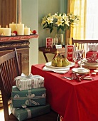 Weihnachtspäckchen auf Stuhl neben Esstisch mit Geschirrstapeln auf roter Decke