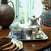 Silbertablett mit blau/weissen Bechern und silbernem Teeservice neben Metallvase auf Esstisch