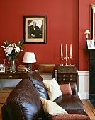 Braunes Ledersofa im traditionellem Wohnzimmer mit Schwarzweiss-Portrait auf roter Wand