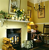 Holzscheite und Geschenke neben dem brennenden Kamin in traditionellem, cremefarbenem Wohnzimmer