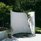 Kleiner Springbrunnen vor weisser gebogener Wand auf der Terrasse