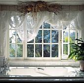 Getrocknete Blüten am Balken und weiße Voile Vorhänge am Fenster über der Badewanne