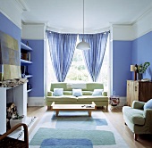 Lindgrünes Sofa vor dem Erkerfenster mit blauen Gardinen