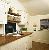 Cremefarbene Küchenzeile mit hölzerner Arbeitsplatte und Schiefertafel über dem Spülbecken