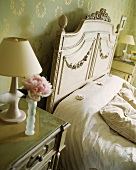 Ein Nachttisch neben einem cremefarbenen Bett in einem Schlafzimmer mit grün gold Tapete
