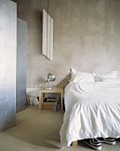 Bett mit weisser Bettwäsche neben dem Metall-Parvent in einem Schlafzimmer mit Betonwänden