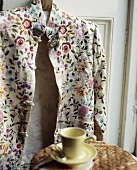 Eine cremefarbene bestickte Jacke hängt an der Tür hinter einem Tisch mit Tasse