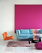 Ein blaues Sofa vor einem pinkfarbenem Bild in einem Wohnzimmer