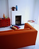 Rotes Sofa und Schränkchen in einem weissen Wohnzimmer mit Kamin