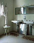 Badezimmer mit zwei Waschbecken, rechteckigem Spiegel, kleinem Metalltisch und altem versilberten Spiegel unter den Waschbecken