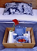 Holztablett mit blauer Teekanne und Tassen auf einem Bett mit blau-weisser Bettwäsche