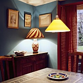 Blaue Esszimmerecke mit brennender, dekorativer Tischlampe und gelber Pendelleuchte über Tisch