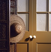 Farbklang von Karamell bis Mahagoni - Strohhut an filigranem Wandschirm neben verglaster, verhangener Tür