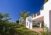 Garten mit Palmen und Rasen vor einer modernen weissen spanischen Villa mit Balkon