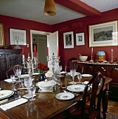 Silberwaren und Porzellan auf dem antiken Tisch in einem roten Landhaus-Esszimmer