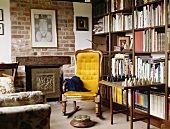 Gelber Sessel und Schach auf dem Tisch vor Bücherregalen eingerichtet im Landhaus Wohnzimmer mit Kamin in exponierter Mauer