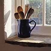 Ein blauer Keramikkrug mit Holzgeschirr steht auf einer Fensterbank