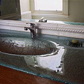 Ein Detail einer Glasplatte, in der ein rundes Waschbecken eingelassen wurde