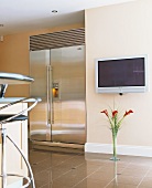 Grosse Kühl-/Gefrierkombination aus Edelstahl im amerikanischen Stil neben Flatscreen-Fernseher an der Wand in moderner Küche