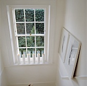 Weisser Landhaus-Treppenabgang mit Reihe gleicher Vasen vor altem Sprossen-Schiebefenster