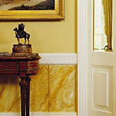 Traditioneller Eingangsflur mit Reiterskulptur auf antikem Tischchen vor marmorvertäfelter gelber Wand