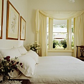 weiße Decke und Kissen auf Doppelbett in cremefarbenem Schlafzimmer mit Blick in den Garten durch drapiertem Vorhang