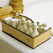 weiße Flaschen in rustikalem Holzkästchen und Bastdosen auf der Fliesenumrahmung einer Badewanne