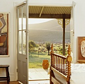Antikes Holzbett mit gedrechselten Spindeln in weißem, australischem Schlafzimmer mit Blick durch offene Tür in die Landschaft