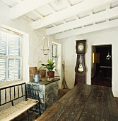 Esszimmer in altem, bäuerlichen Landhaus mit weissen Holzbalken, geschlossenen Fensterläden und antiker Standuhr neben Tür