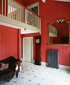 Galerie mit cremefarbenem Holzgeländer über antiker Standuhr und goldgerahmtem Spiegel in Wohnraum mit roten Wänden und kühlem, weißem Fliesenboden