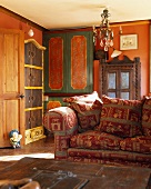 Rot-gemustertes Polstersofa in Wohnzimmer mit verschiedenen bemalten Schränken vor orangefarbenen Wänden
