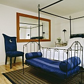 Ein Tagesbett mit Metallgestell und blau gestreiften Kissen am Fussende eines schwarzen Himmelbettes