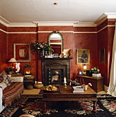 Rot gemusterte Tapeten und eine grosser Teppich mit Blumenmotiv in einem Wohnzimmer mit Kamin