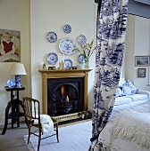 Schlafzimmer mit offenem Kamin aus Kiefernholz, traditionellem Himmelbett mit Willow-gemusterten Vorhängen und blau-weissen Porzellantellern über dem Kamin