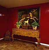 Großes Ölgemälde mit Hundemotiv über einer antiken Anrichte hängend, in einem Saal mit rotlackierten Wänden