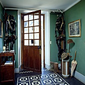 Diele in Grün mit schwarz-weiss gefliestem Boden, hängendem Zaumzeug und einer offenen, halb verglasten Tür