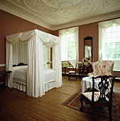 Schlafzimmer in einem Landsitz mit Himmelbett mit weißen Vorhängen, Parkett und ornamentaler Stuckdecke