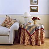 Runder Tisch mit rot-weiss-blau gemusterten Decken neben einem weissen Sofa in einem Wohnzimmer
