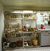 Offenes Metallregal mit Vorratsgläsern und verschiedenen Lebensmitten in einer Küche