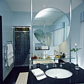 Ein Runder Spiegel über dem Glasregal und dem schwarzen Waschtisch in einem modernen Bad