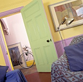 Blick aus einem Wohnzimmer mit gelber Wand und grüner Tür auf den Gang