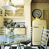 Runder Glastisch mit Metall-Stühlen und ein frei stehender Kühlschrank in einer cremefarbenen Küche