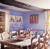 Kelim-Teppich auf Tisch mit rustikalen Holzstühlen und geschwungener Lehne im blau getönten Esszimmer