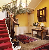 Gelbgetönte Eingangshalle mit Orientteppich und Wandtisch neben Treppe mit rotem Teppichläufer