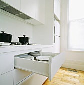 Moderne weiße Küche mit offener Schublade und eingeräumten weissen Tellern