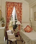 Einzelbett mit weisser Decke und rot-weiss gemusterte Vorhänge in einem Gästerzimmer