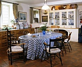 Antike Stühle um den Tisch mit blau-weiss karierter PVC-Tischdecke in einem Landhausküche