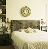 Bett mit geschnitztem Kopfteil und antiker Wanduhr im schlichten Schlafzimmer