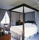Himmelbett mit dunklem Holzgestell und weiss blau gestreiften Vorhängen im weiss blauen Schlafzimmer